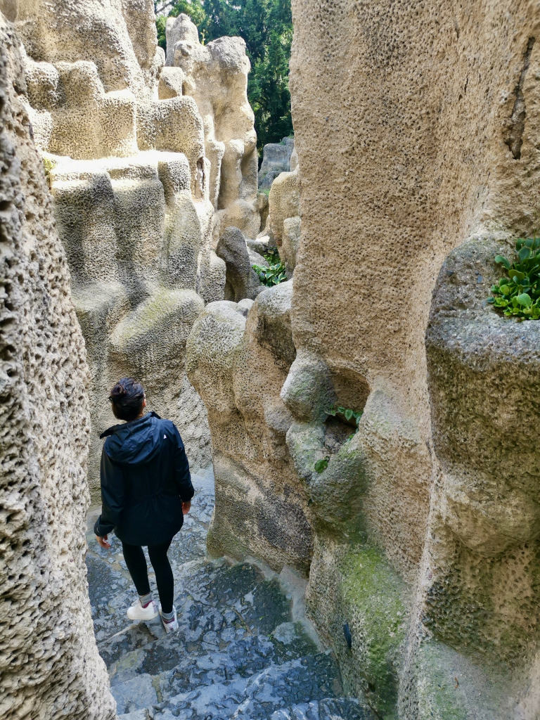 A woman in a black jacket and black tights walking down some stairs in an artificial cave 