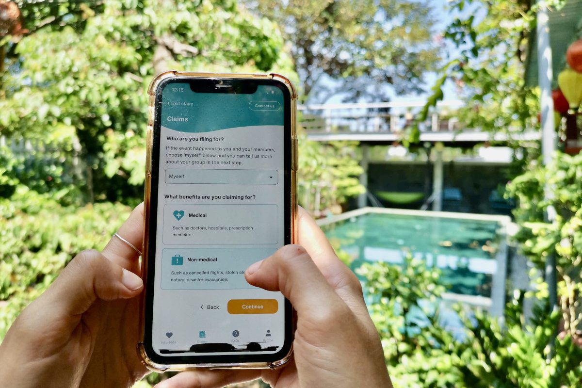 A hand holding a phone next to a pool surrounded by grennery with the SafetyWing App on the screen