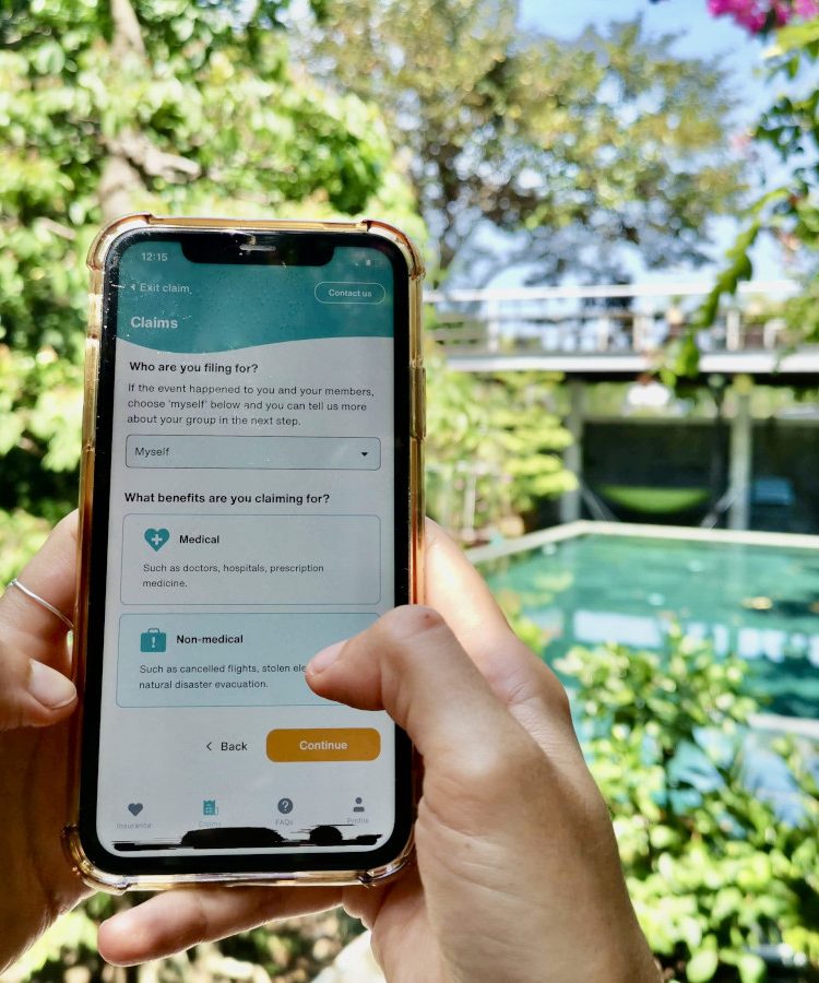 A hand holding up a phone next to a pool surrounded by grennery with the SafetyWing App on the screen.