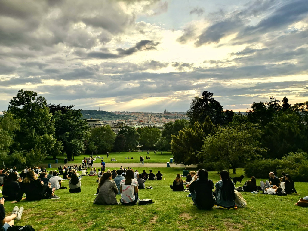 A group of people sitting on a grassy hillside watching the sunset over prague