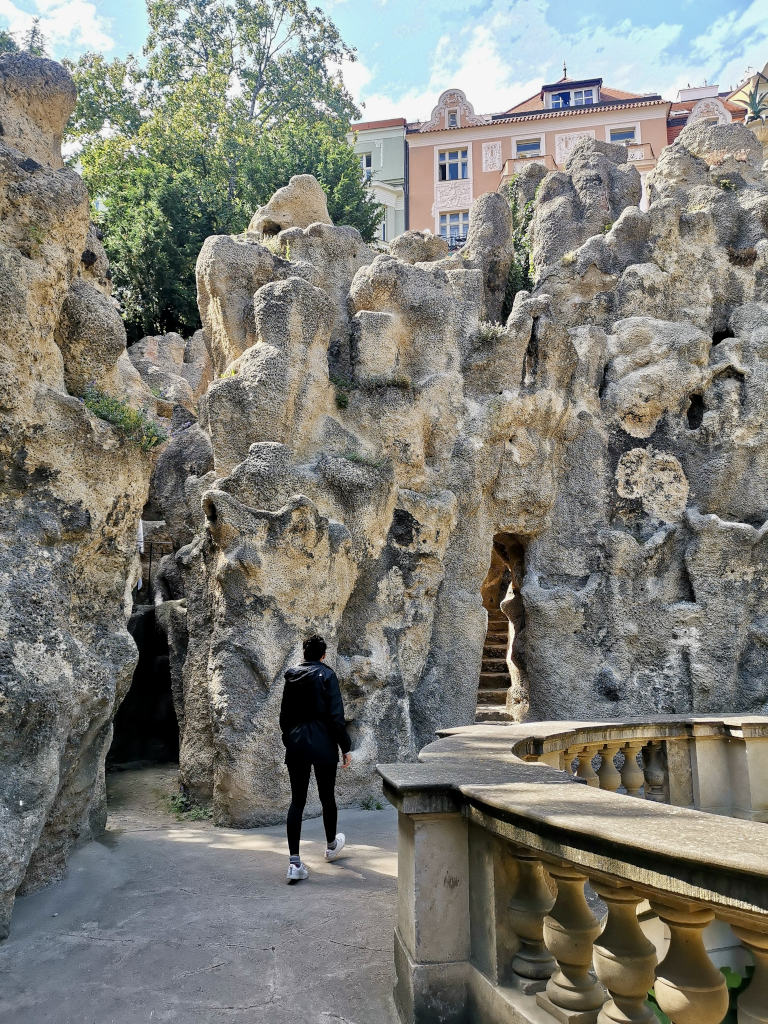 A woman walking along a walkway in front of the grotto an artificial cave that is great to visit on a prague itinerary