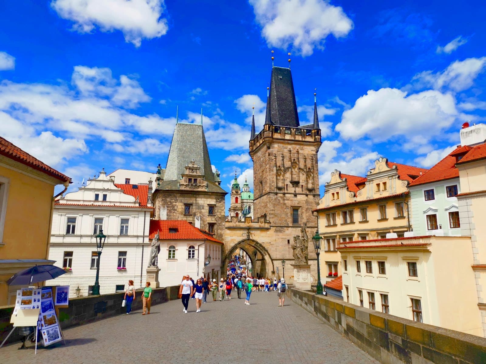 Tourists walking across the Charles Bridge through a city gate tower towards Prague Castle.