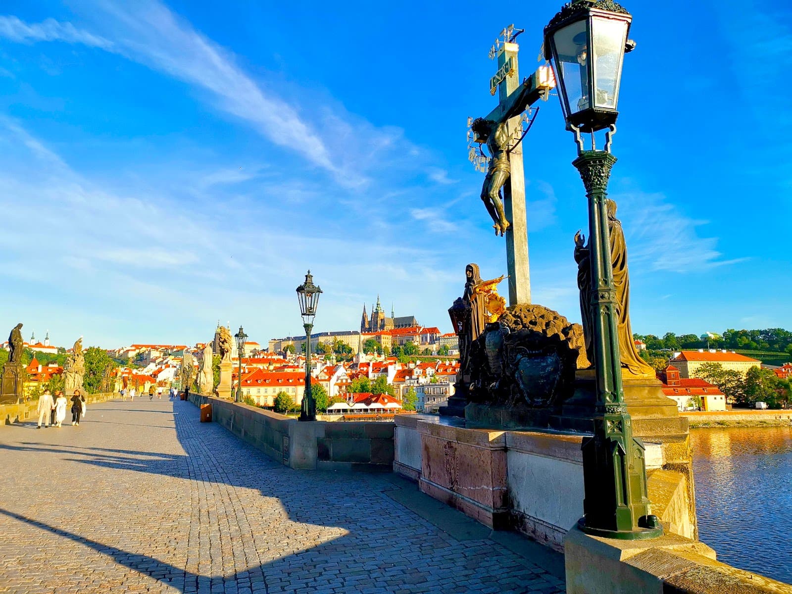 Few people walking across the Charles Bridge just after sunrise which is a great start of your Day 2 Prague itinerary.