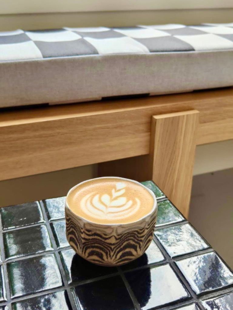 A cup of flat white with milk foam shaped like a flower on a black tiled coffee table at Clay Cafe.