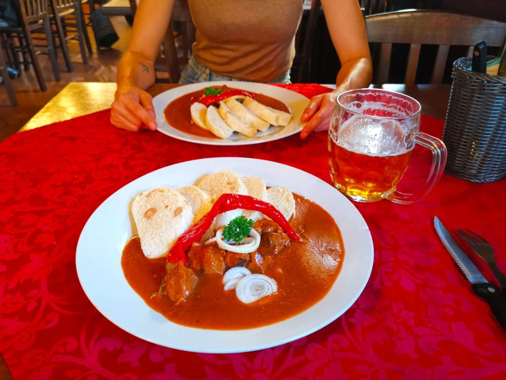 Two plates with red goulash and five slices of dumplings on a red table cloth served in a traditional Czech restaurant in Vinohrady. 