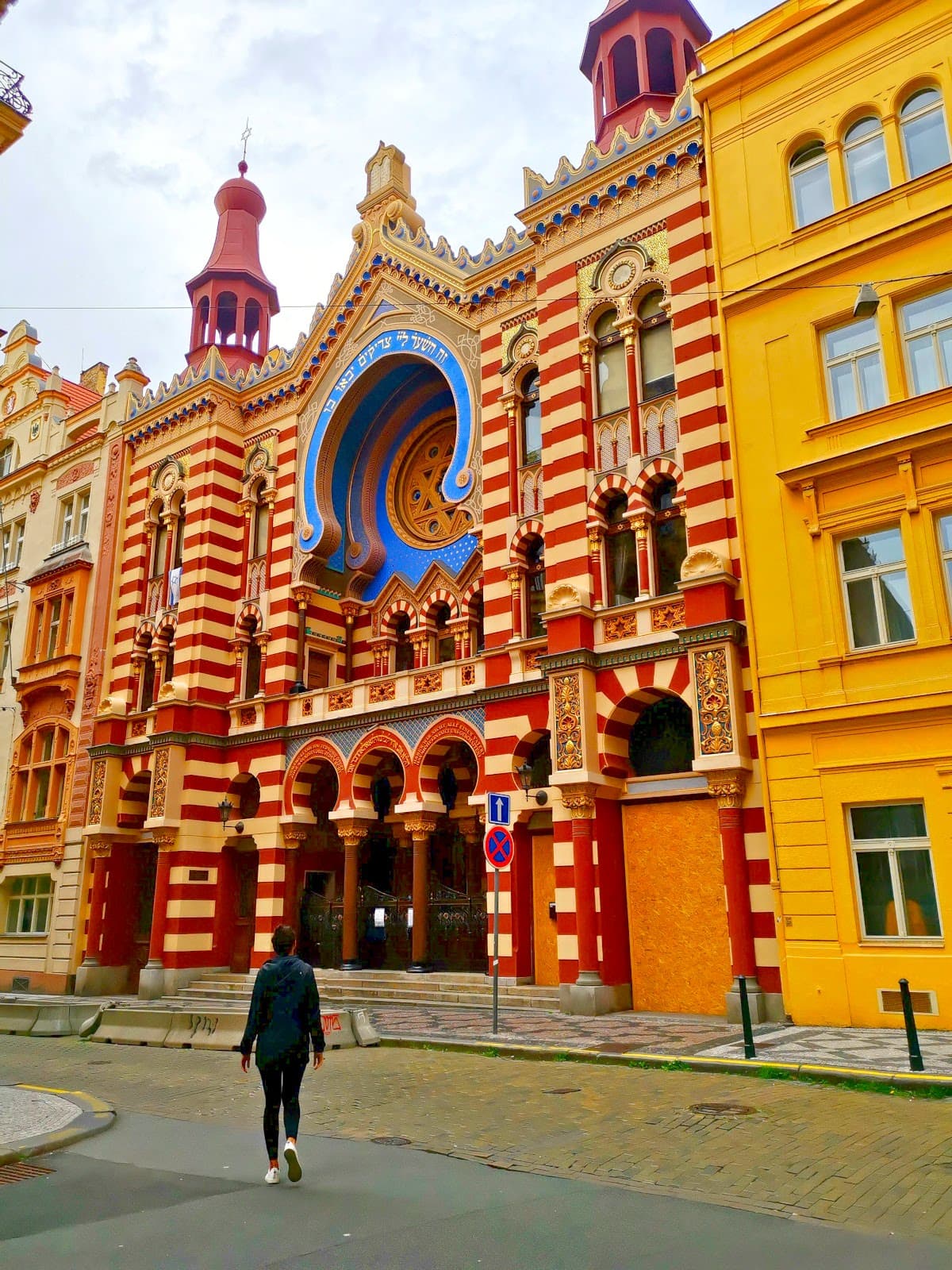 Katharina walking towards the Jerusalem Synagogue in Prague with an impressive colorful exterior of red stripes and a blue archway.