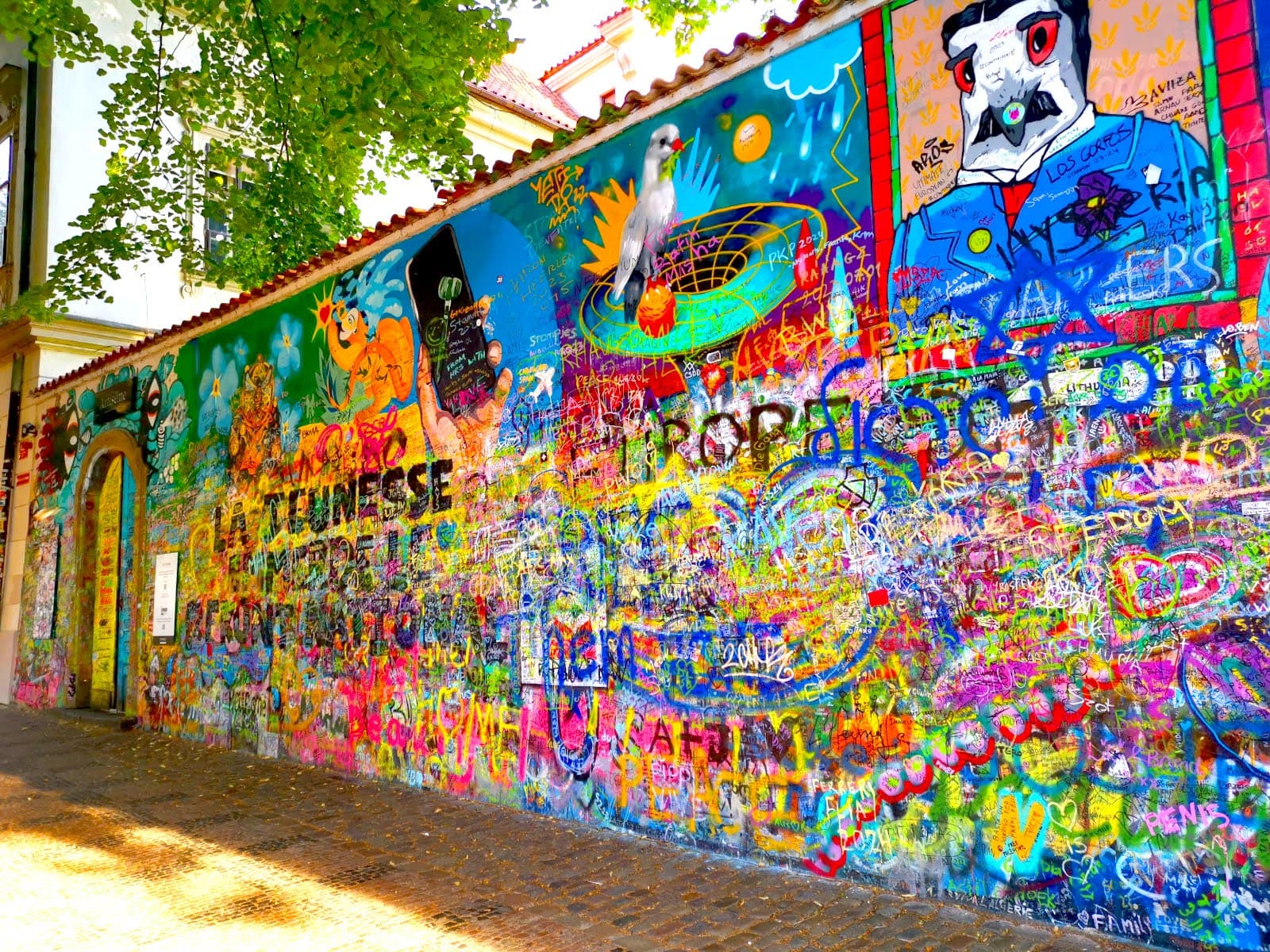 John Lennon Wall Prague with colorful graffiti, symbols and writtings layered on top of each other.