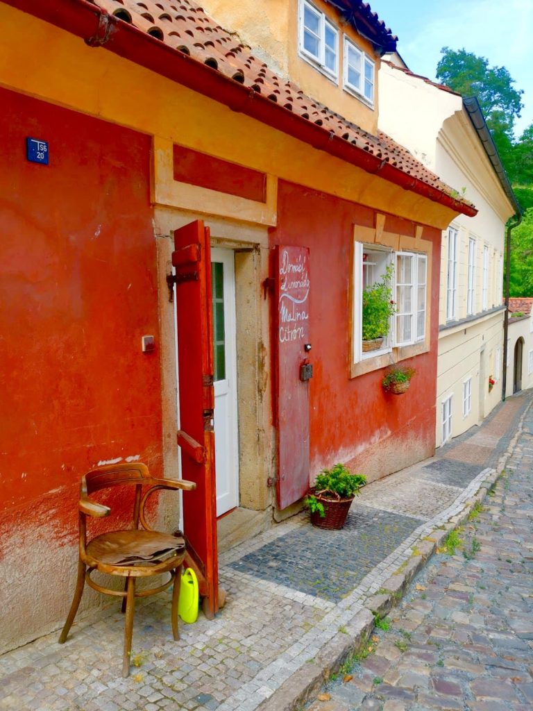 A red colored house in Malá Strana with a wooden chair outside.