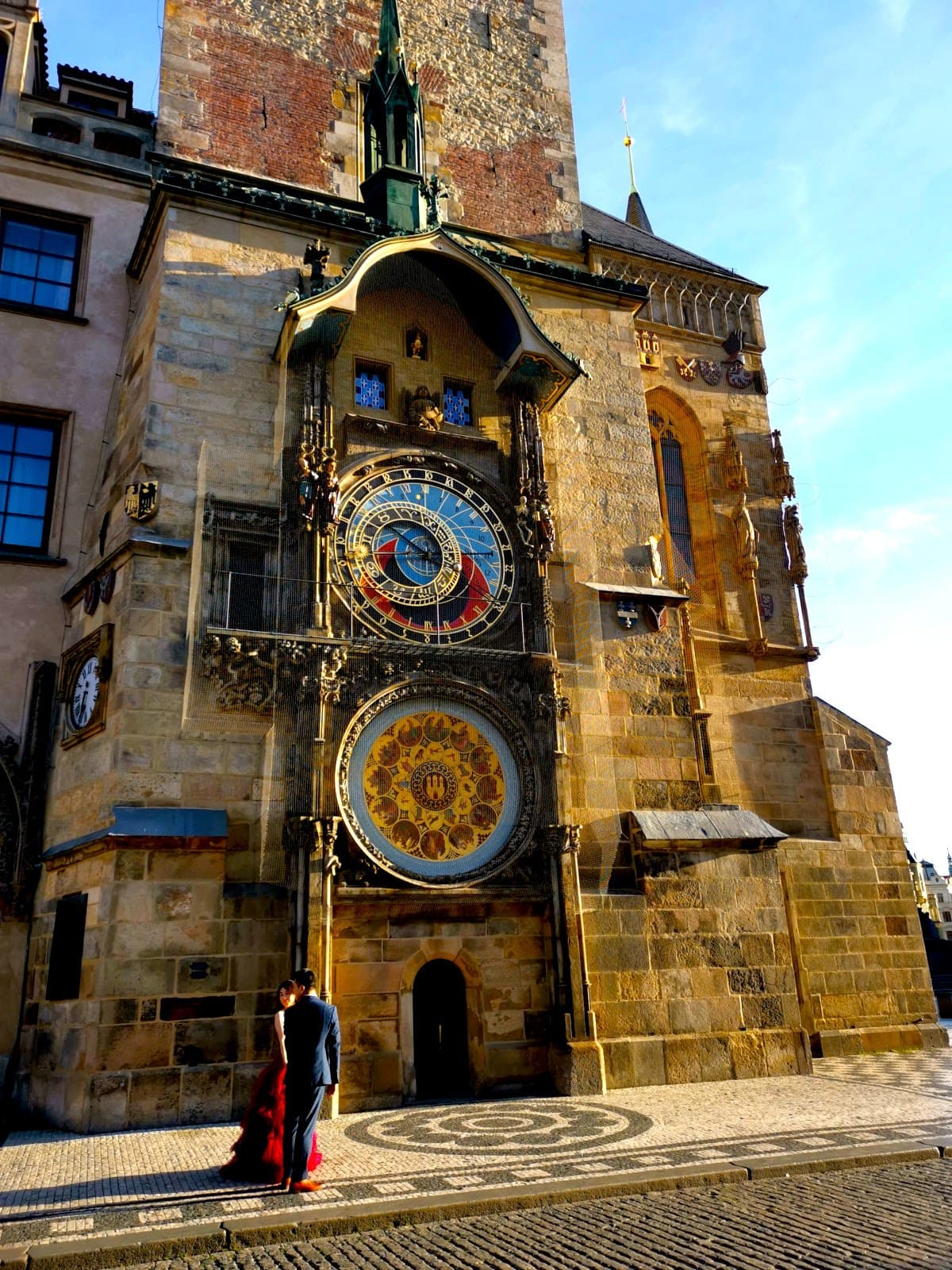 A couple in a red dress and blue suit posing in front of Prague's Astronomical Clock.