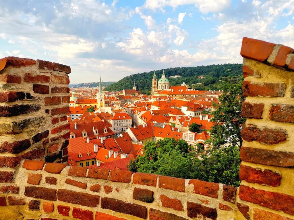 View over red roofs and church towers of Malá Strana framed with the brick walls of Prague Castle.