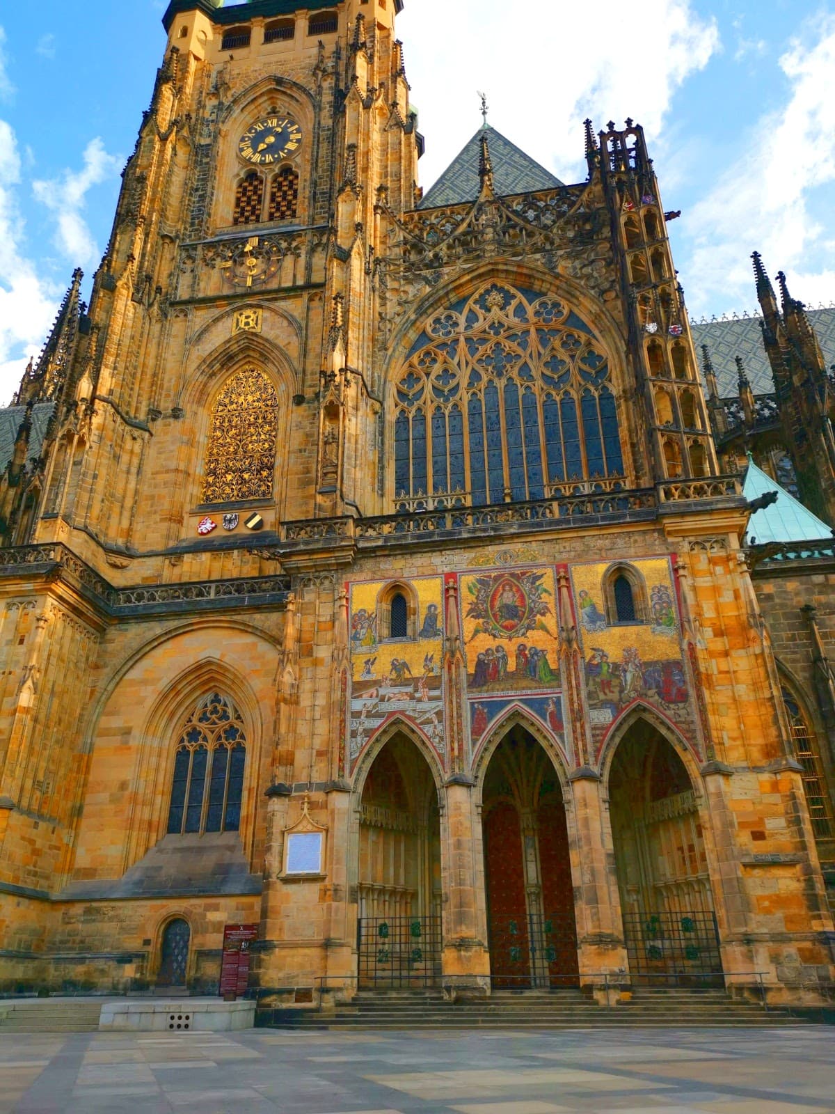 The side front of St. Vitus Cathedral of Prague Castle with colorful religious murals and gothic windows.