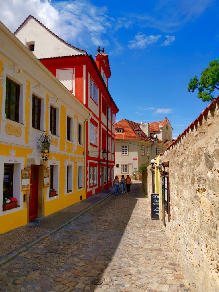 Nový Svět, a cobblestone street with colorful houses in Malá Strana, Prague with people walking on it.