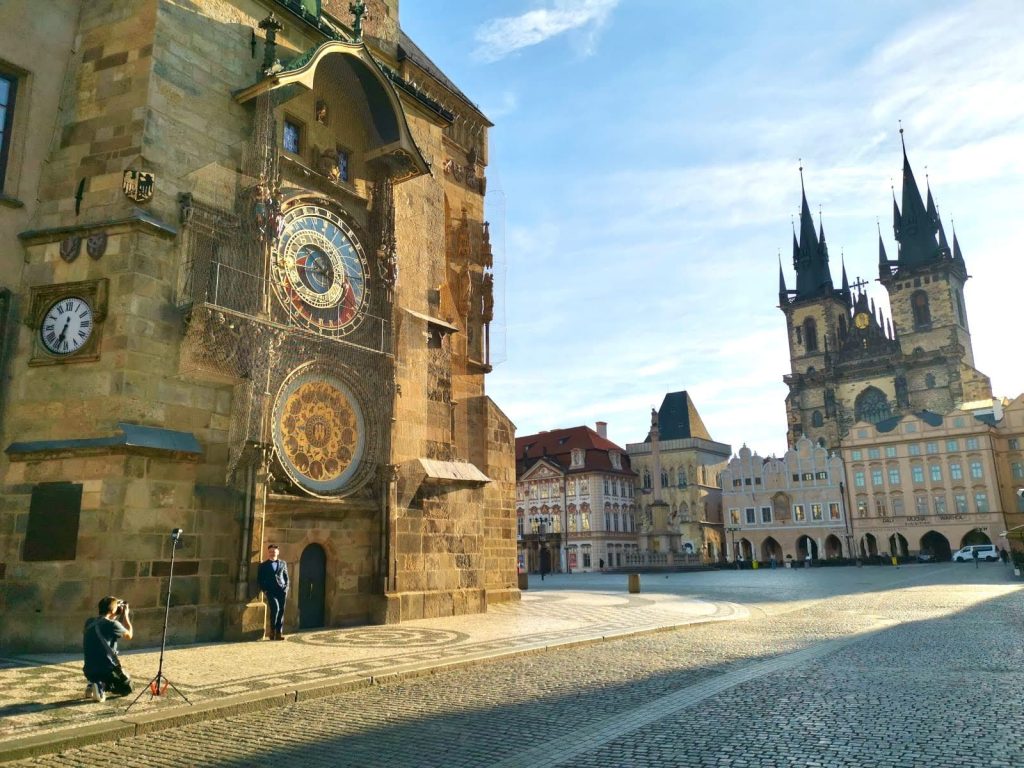 Empty Old Town Square with a photographer taking a photo of a man posing in a suit in front of Prague's Astronomical Clock.