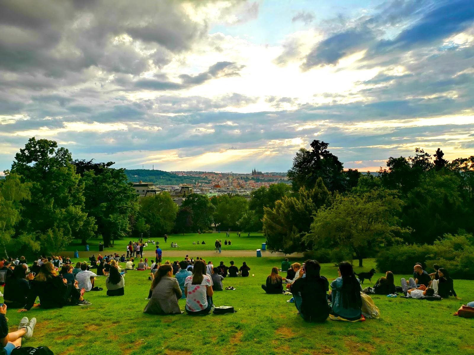 A group of people sitting on a grassy hillside watching the sunset over Prague in Riegrovy Sady Park.