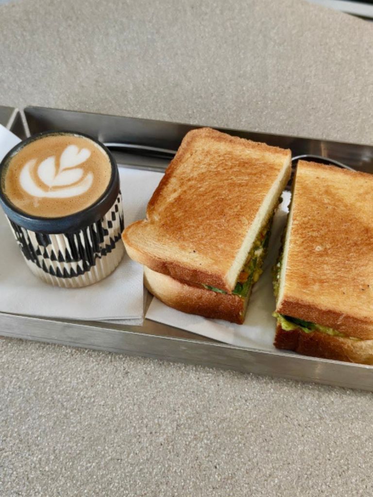 A flat white coffee and a toastie on a metal tray at The Block Cafe.