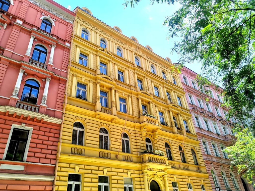 Row of pink and yellow five-story houses next to a green tree in Vinohrady, Prague.