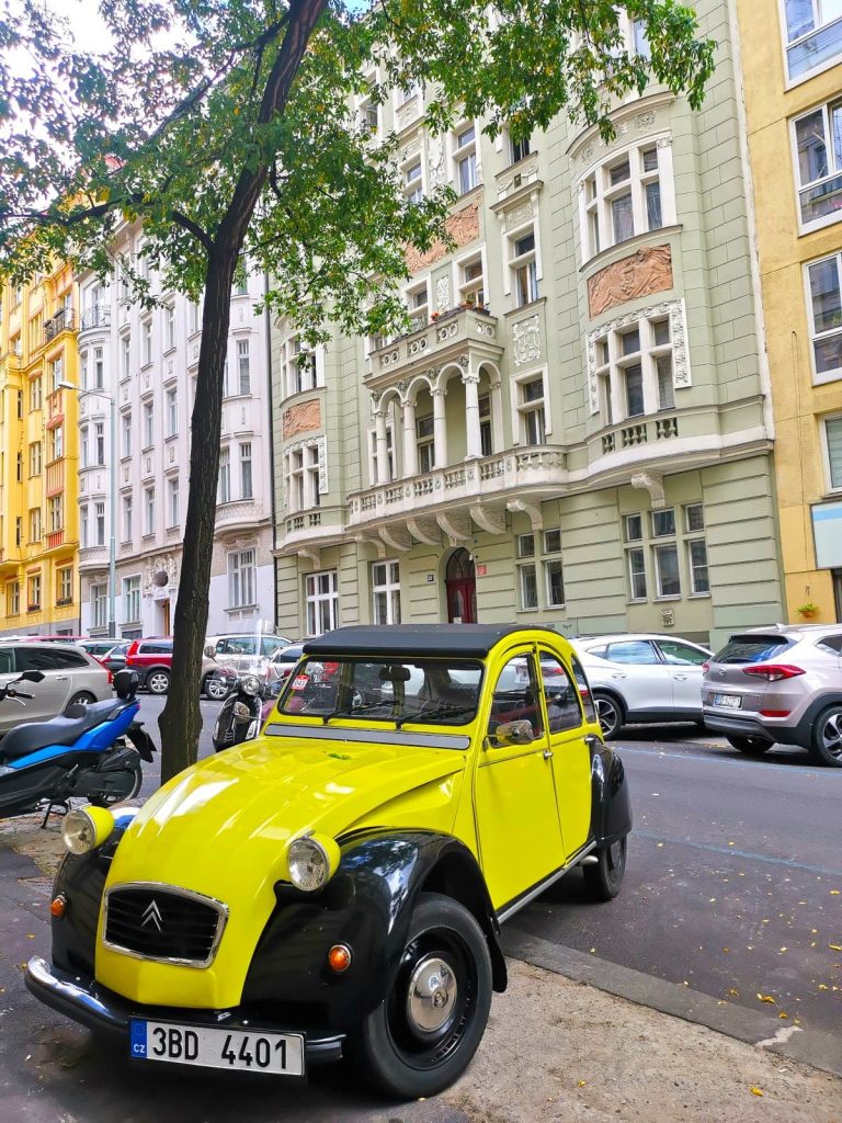 Bright yellow old car parked on a typical local street with high colorful buildings in Vinohrady.