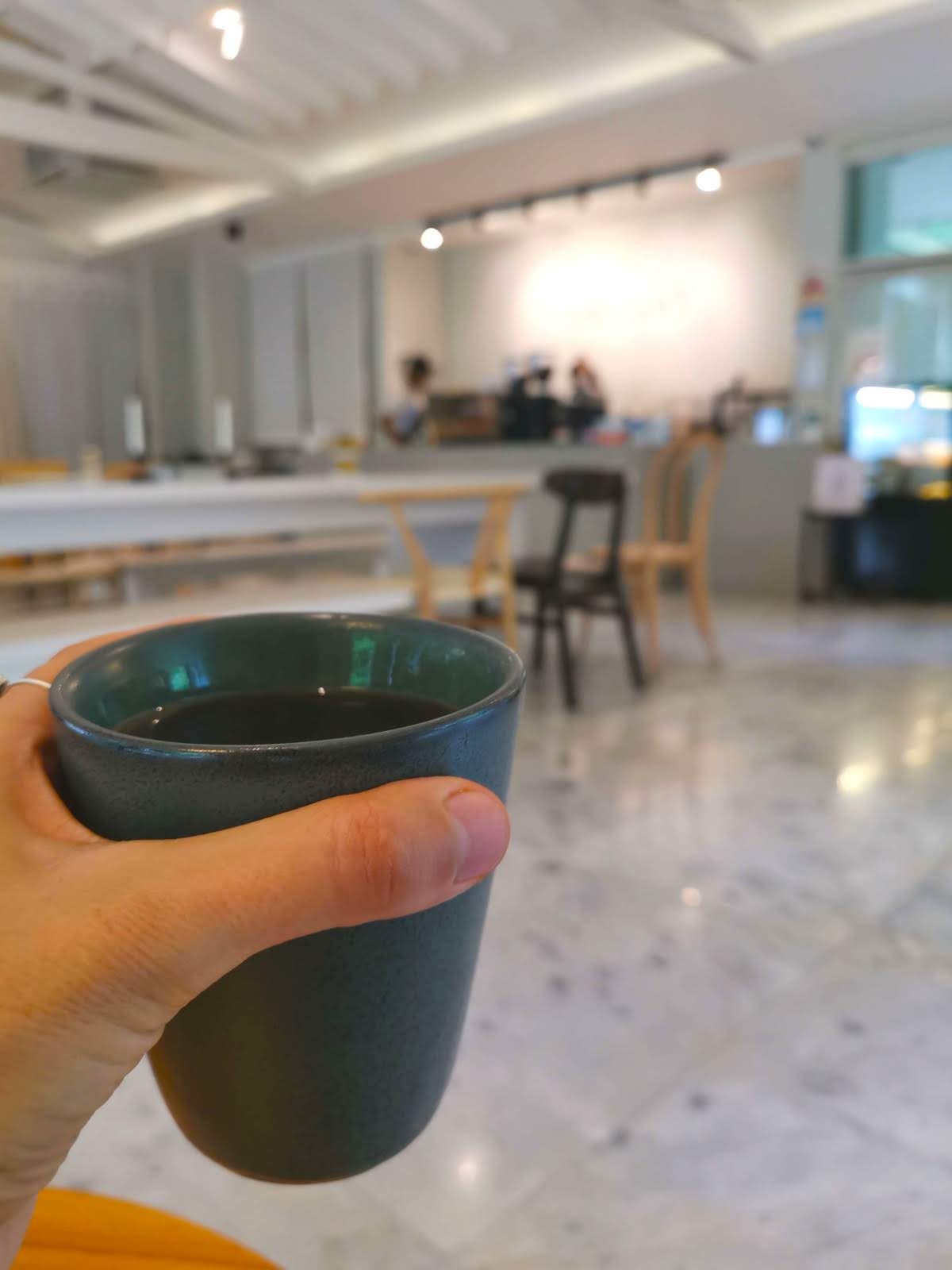 Hand holding a green ceramic cup with a long white co-working table in the background.