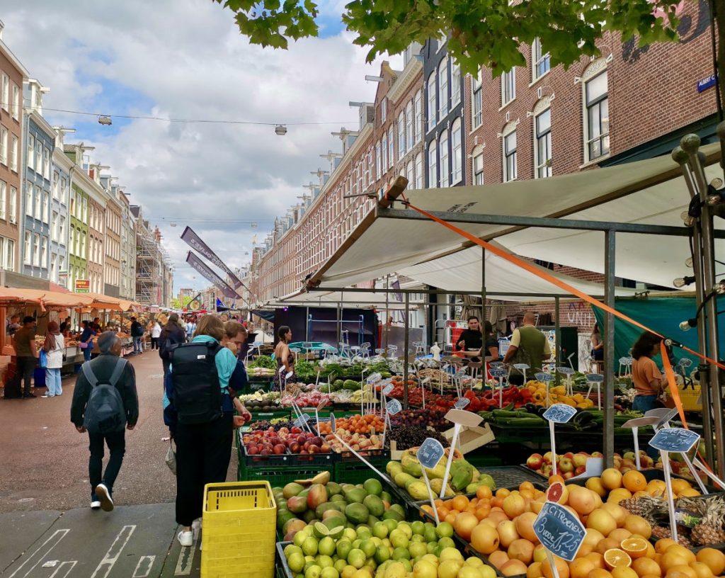 A stand of fruit at a market in amsterdam with people looking at what fruit to buy