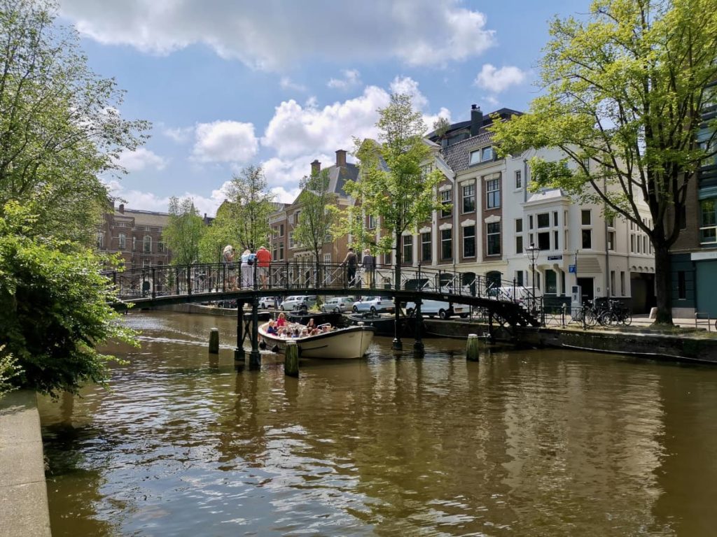 A boat going underneath a small footbridge while a small group of people look down at the boat in amsterdam