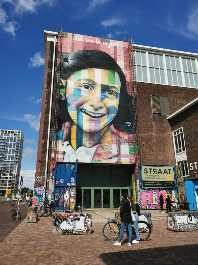 A colorful mural of Anne Frank on the wall of a building in Amsterdam