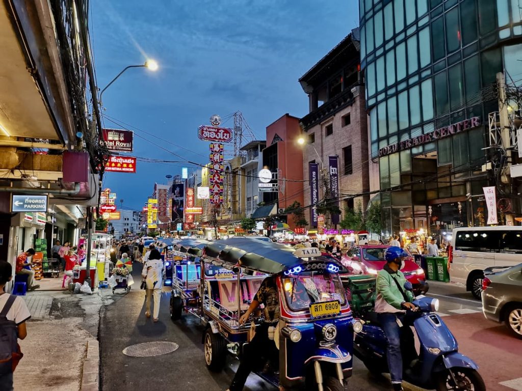 A line of tuktuks, cars and motorbikes driving down the main food street in Bangkok's Chinatown.