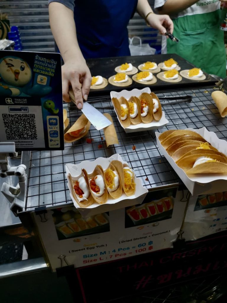 A street vendor preparing crispy coconut pancakes, a popular Chinatown Bangkok street food.