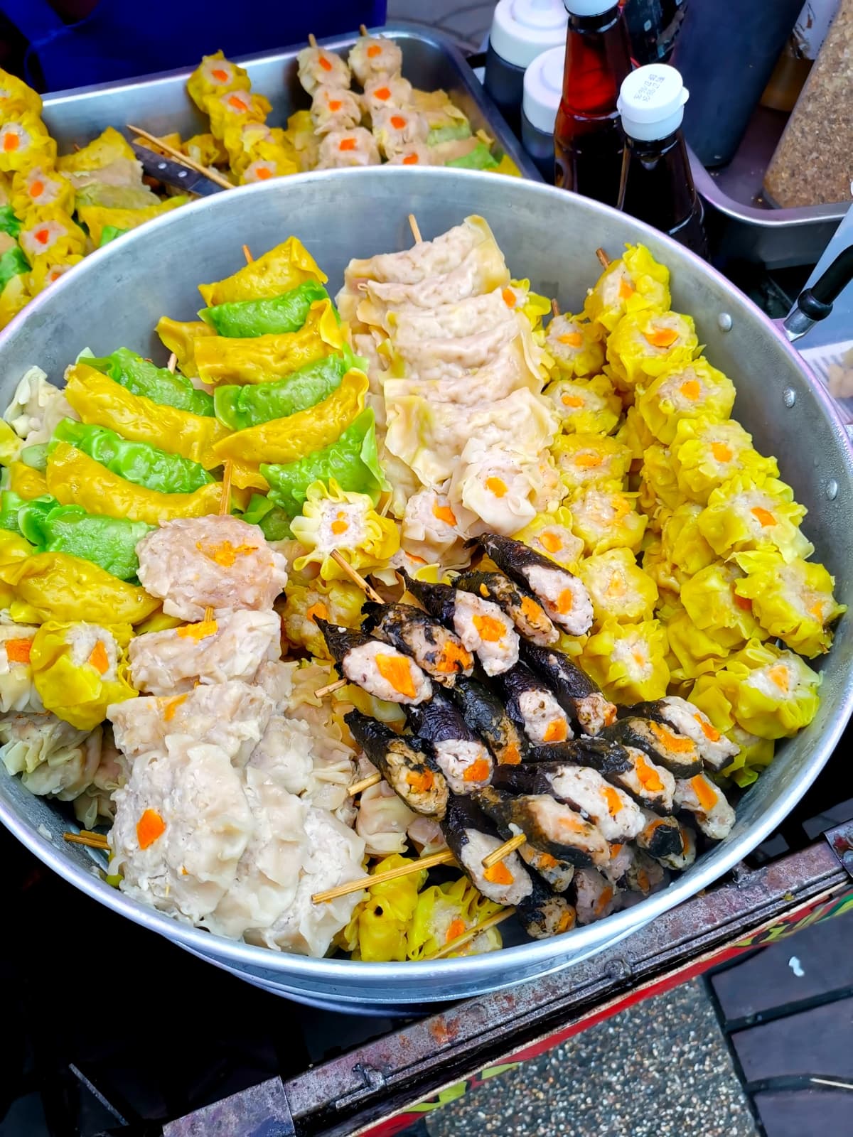 A metal container filled with a variety of white, yellow and green colored dumplings on sticks.