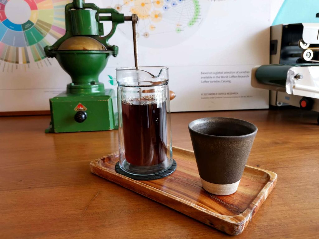 Glass jar of black coffee next to a grey empty coffee cup on a wooden table in Gallery Drip Cafe Bangkok.