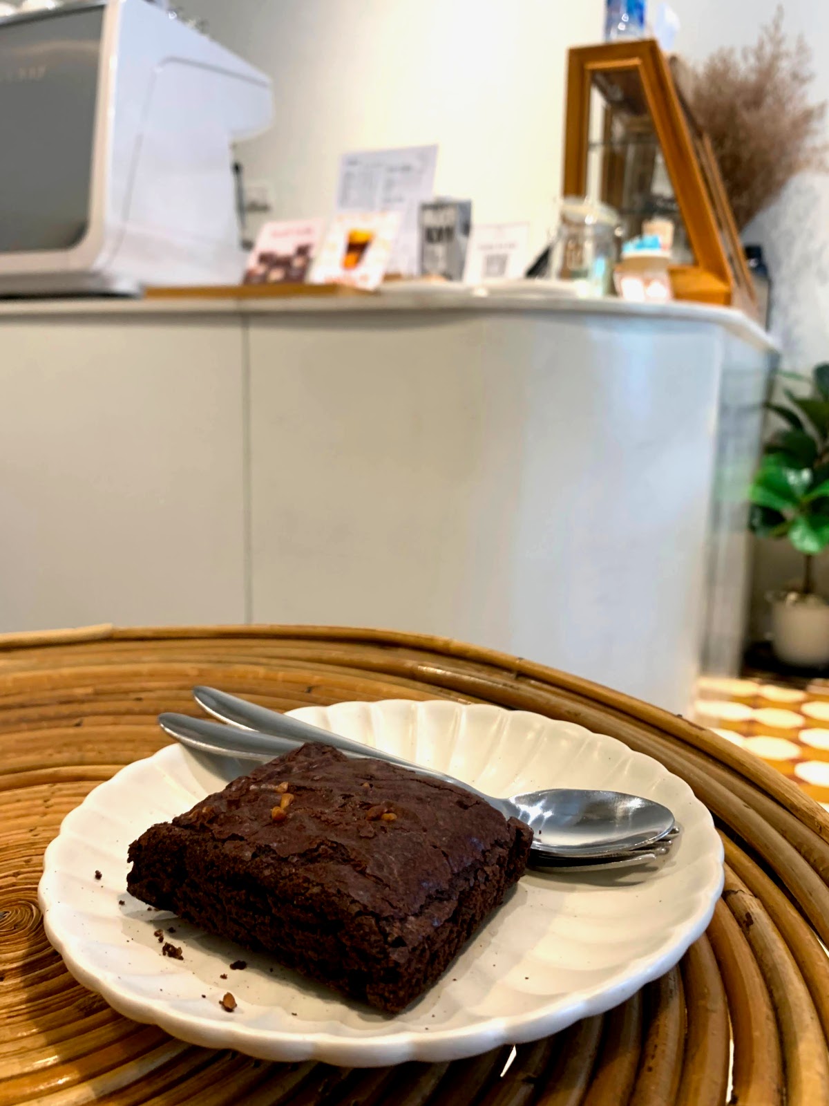 Brownie on a white plate with a spoon and fork beside it, in front of the white coffee bar at Homey Cafe.