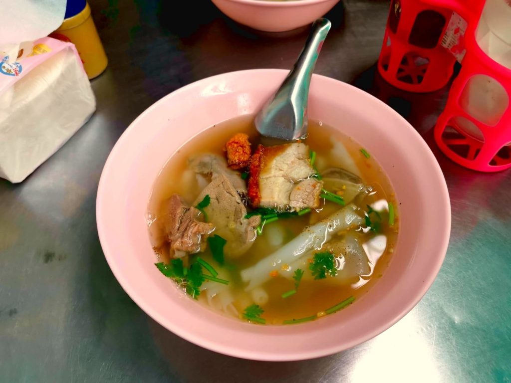 A bowl of soup on a metal table with pieces of pork in it called Kway Chap from Chinatown Bangkok.