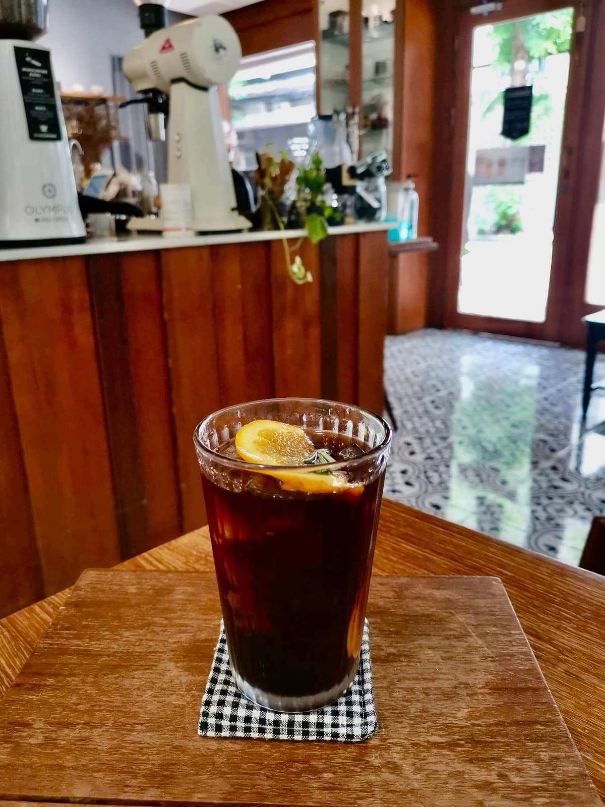 Glass of iced black coffee with an orange slice on a wooden table at Monochrome Cafe in Bangkok.