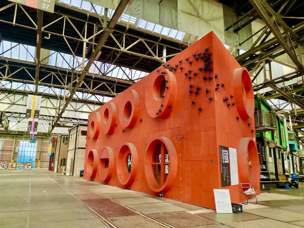 A huge red lego block covered in plastic spiders at NDSM fuse an art gallery that is great to visit as part of an Amsterdam itinerary