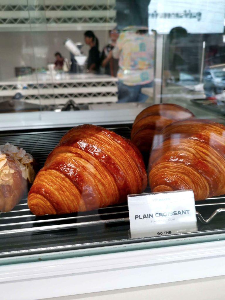 Black tray with golden brown croissants in a glass vitrine.