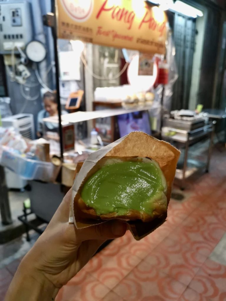 Katharina's hand holding up a paper bag with a white bread bun inside that is filled with a green custard sauce.