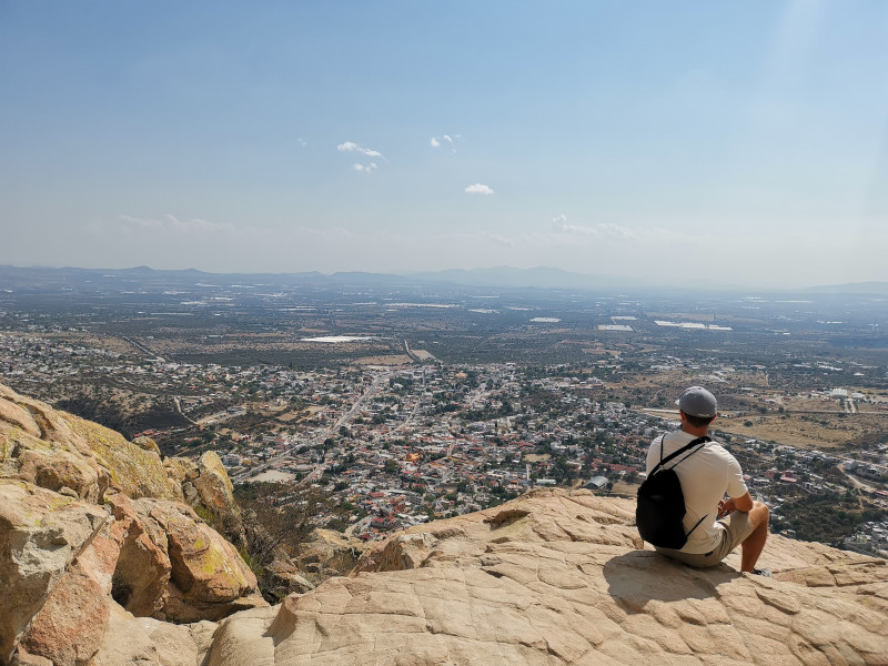 Allan sits on a white rock at Peña de Bernal, Mexico, overlooking the town in the distance.