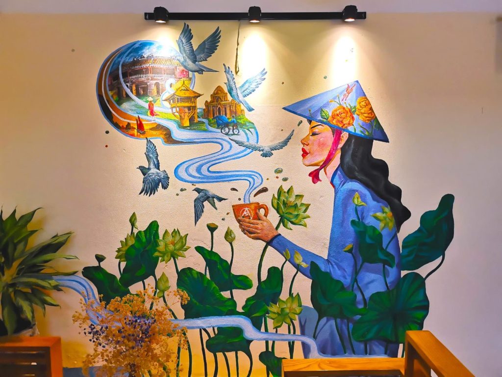 A painted artwork at Art Coffee Hoi An showing a Vietnamese woman in a conical hat enjoying the aroma of a coffee cup, surrounded by vibrant birds and flowers.