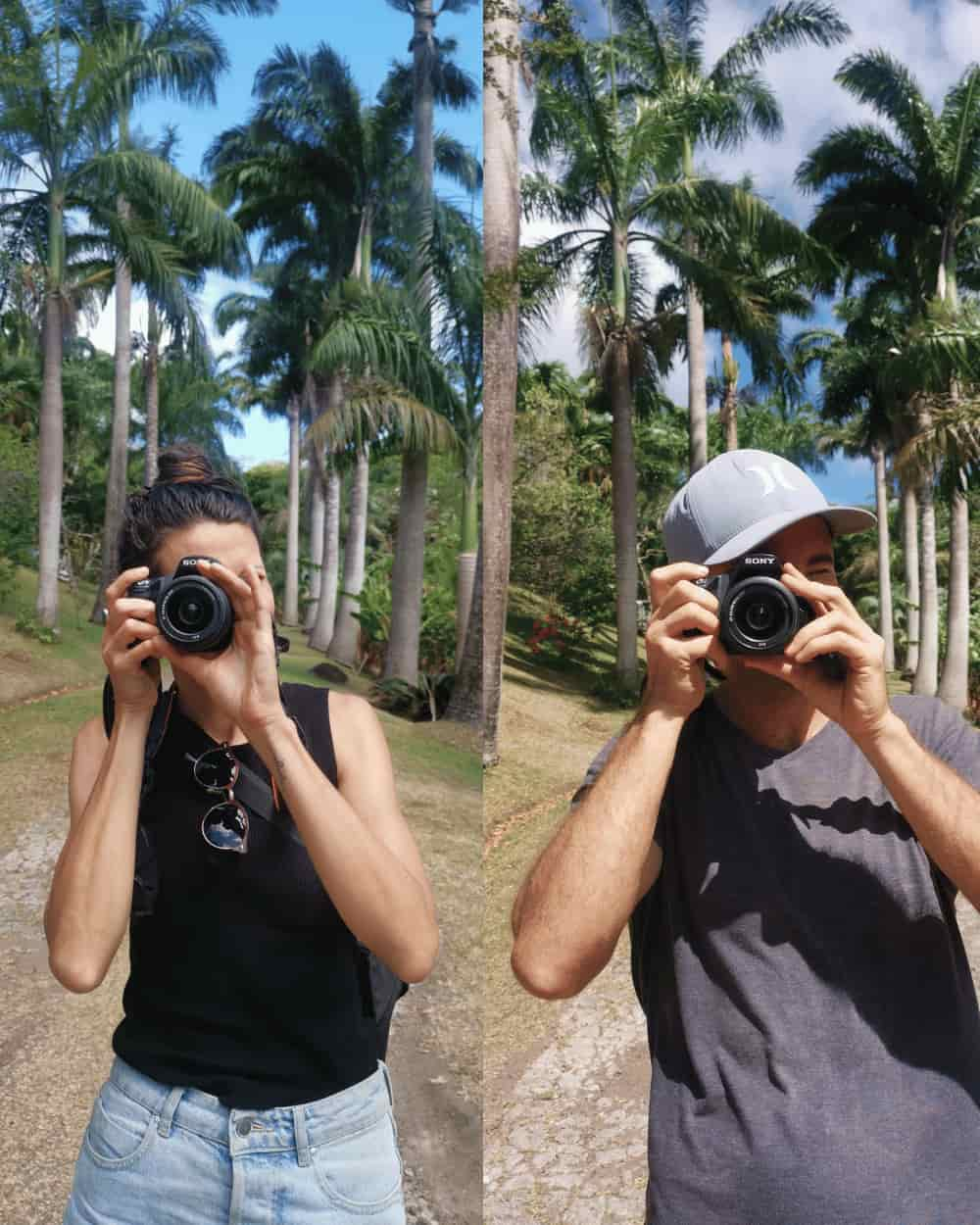 Katharina (Kat) and Allan, the authors behind the travel blog Happy Healthy Nomads, stand side by side with palm trees in the background, holding DSLR cameras in front of their faces.