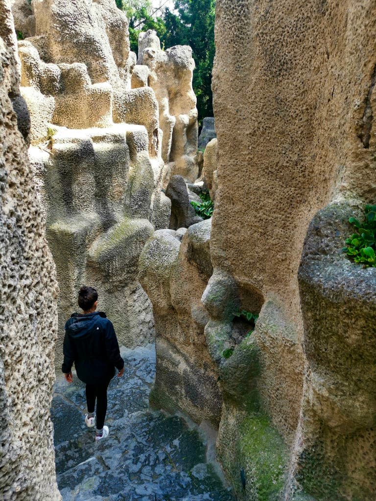 Katharina walks down the stairs, surrounded by beige rocks, in a park in Vinohrady, Prague.