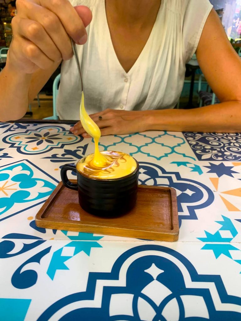 Katharina seated at Phin Coffee Restaurant, holding a spoon with creamy egg coffee dripping back into the cup, one of the best egg coffees in Hoi An.