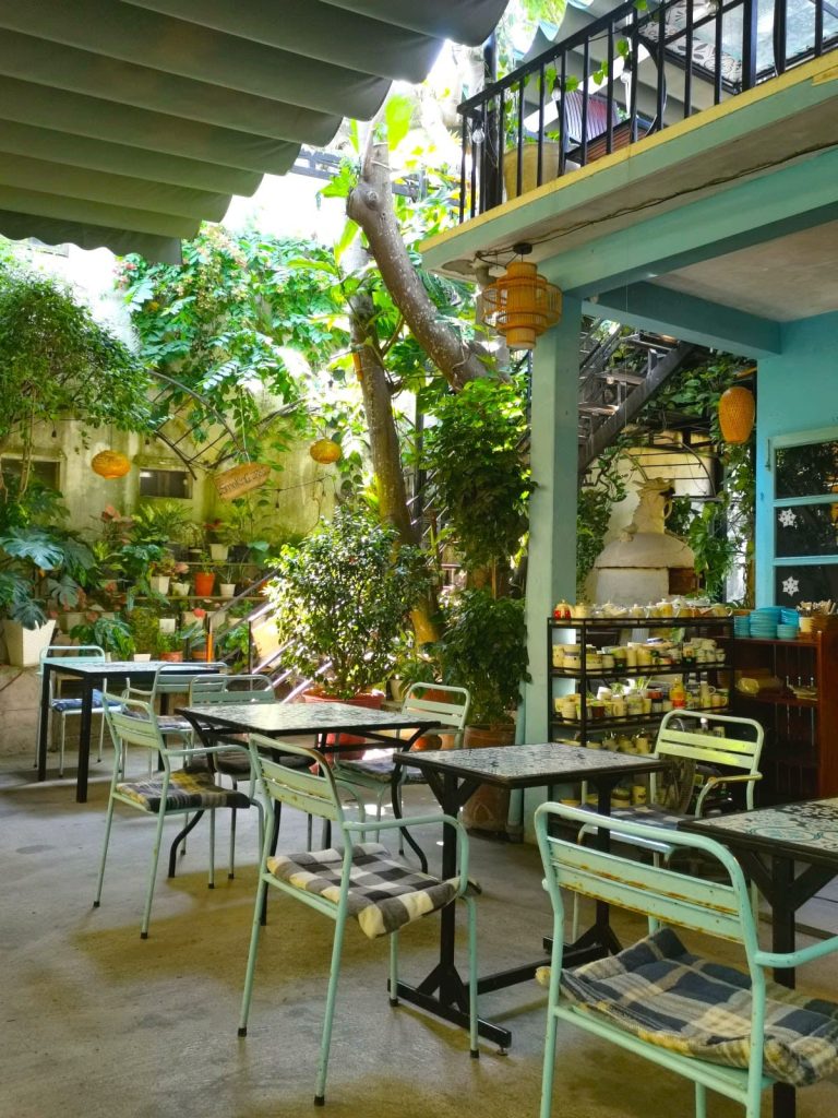 The seating area of Phin Coffee Restaurant in Hoi An with lamps hanging from the roof, plants and light blue metal chairs.