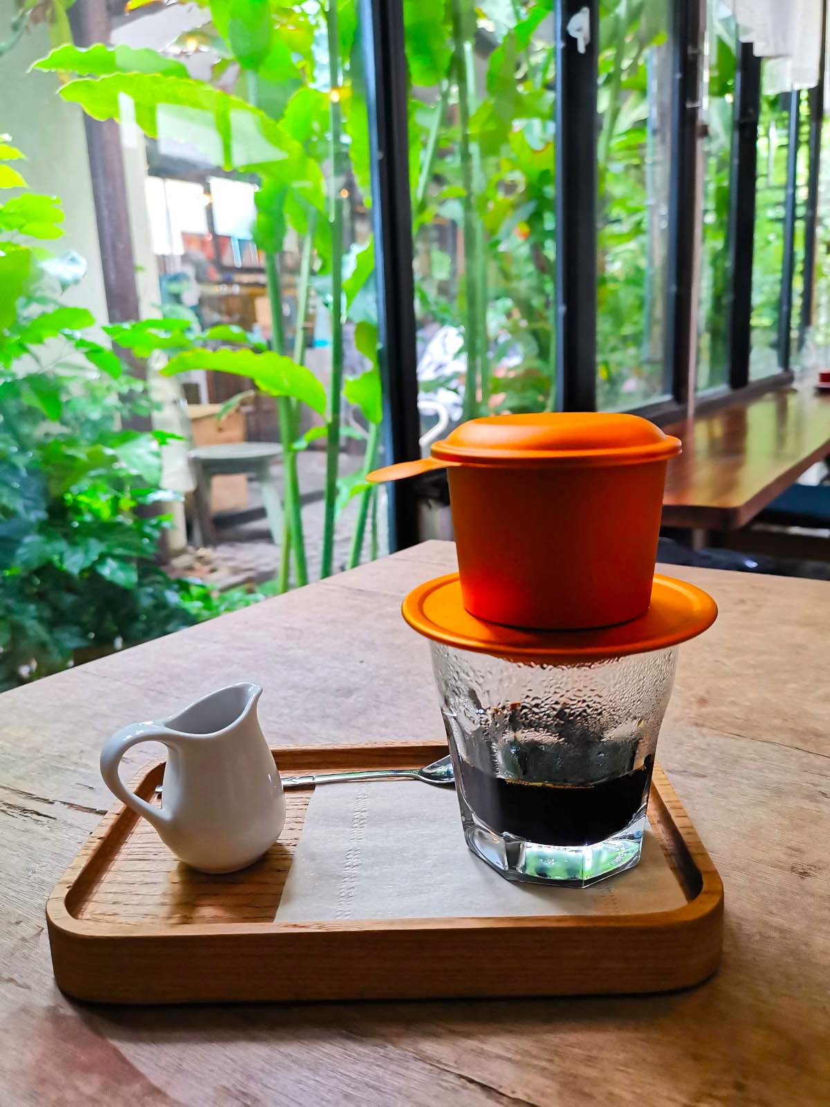 A small glass of black coffee on a wooden tray, topped with a vibrant orange Vietnamese phin filter at the Inner Hoian by Ala cafe.