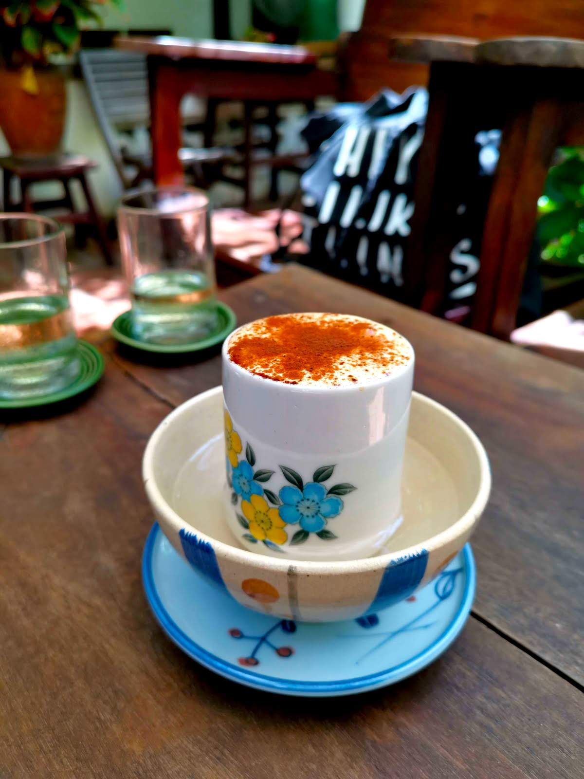 Egg coffee sitting on a table at Ren Rua Cafe in Hoi An. The cup with flowers on it sits in a bowl with hot water.