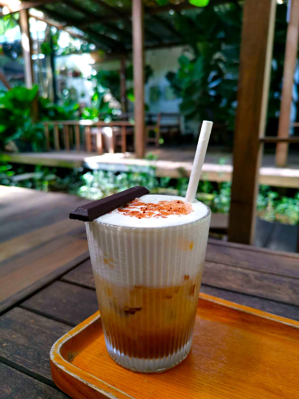 Salt coffee served in a glass on a wooden table, topped with a creamy foam layer, with a white straw and a small piece of dark chocolate placed on top at FeFe Coffee  - one of the best coffee roasters in Hoi An.