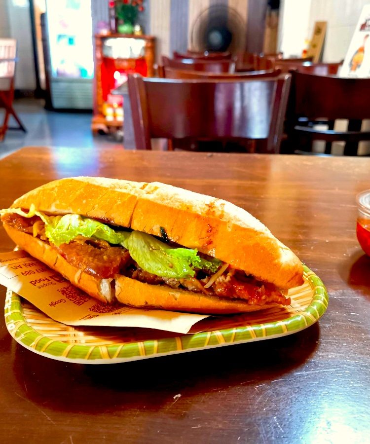 A Vietnamese sandwich filled with meat and lettuce on a wooden table in one of Hoi An's best Banh Mi food places.